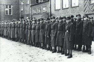 Policjanci w płaszczach wojskowych stoją w kilku rzędach na apelu.