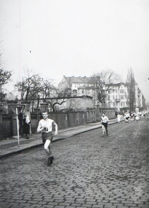 Kilku biegaczy biegnie brukowaną ulicą.